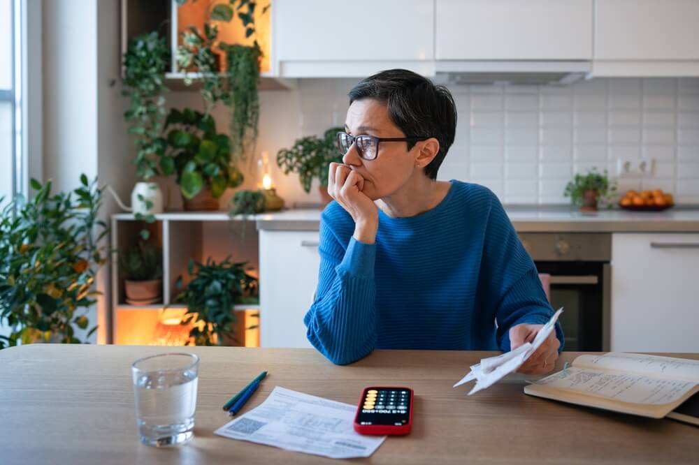 Concerned worried mature woman with bills and receipts, calculating budget and balancing expenses. Female facing debts, mismanagement of funds, rising utility price, tax increase and finance planning