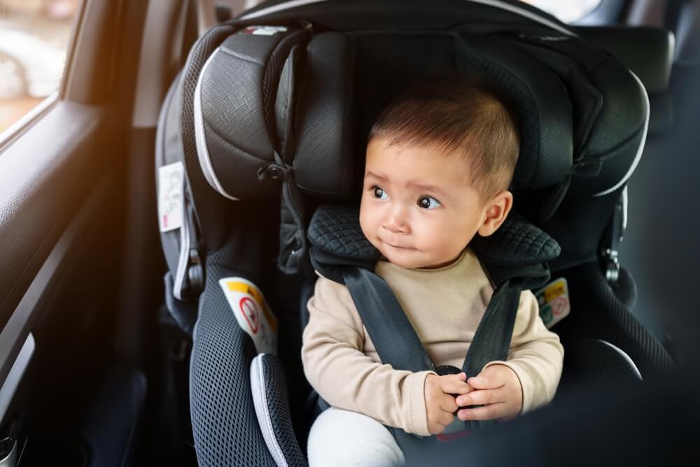 happy infant baby sitting in car seat and looking out of the window.