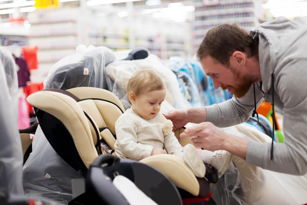 Young father with small daughter choosing car seat in store