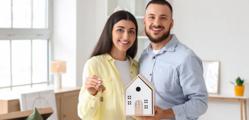 Happy couple holding house keys and a home model, representing homeowners insurance for new homebuyers.