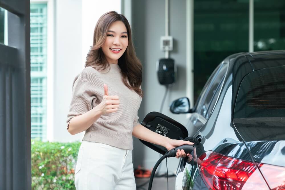 Woman smiles and gives a thumbs-up while charging an electric car, highlighting electric vehicle insurance.