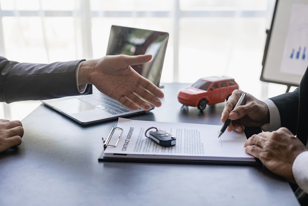 Customer reviewing and signing an auto insurance policy with an agent, illustrating the choice between full coverage and liability car insurance.