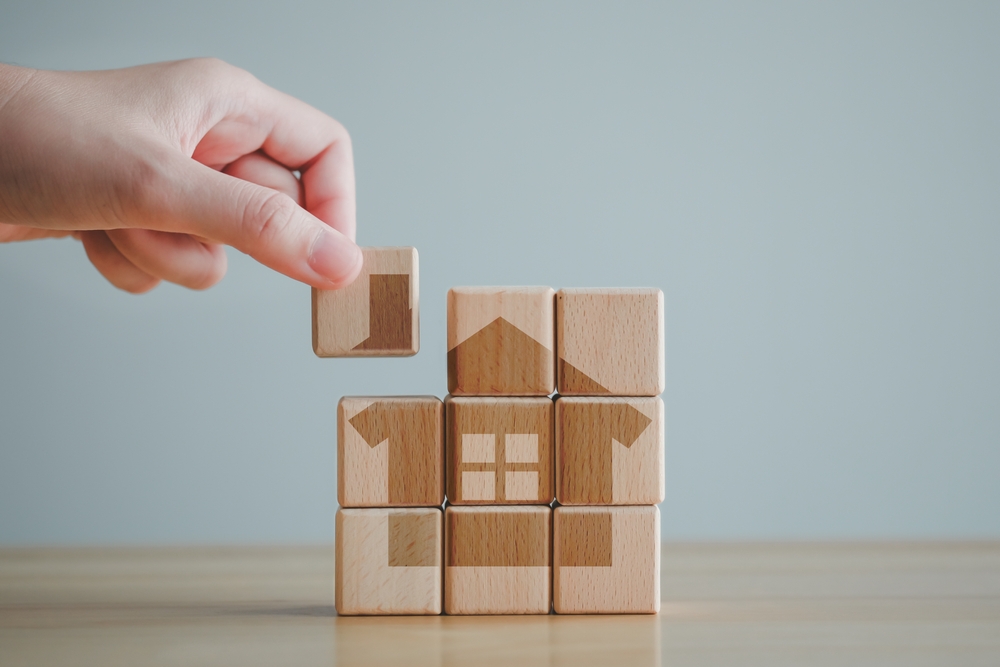 Hand arranging wooden blocks to form a house, representing homeownership and protecting home assets.