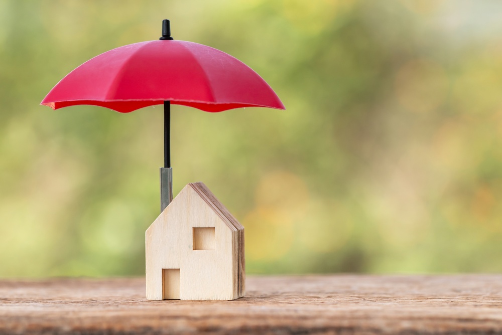 Wooden house protected by a red umbrella, representing umbrella insurance coverage for homeowners.