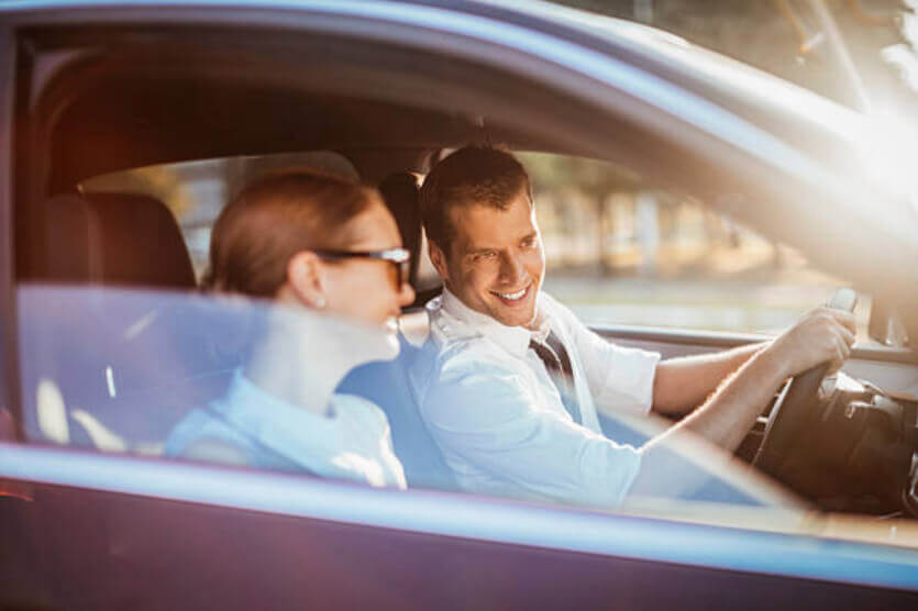 Smiling couple inside of car driving with auto insurance
