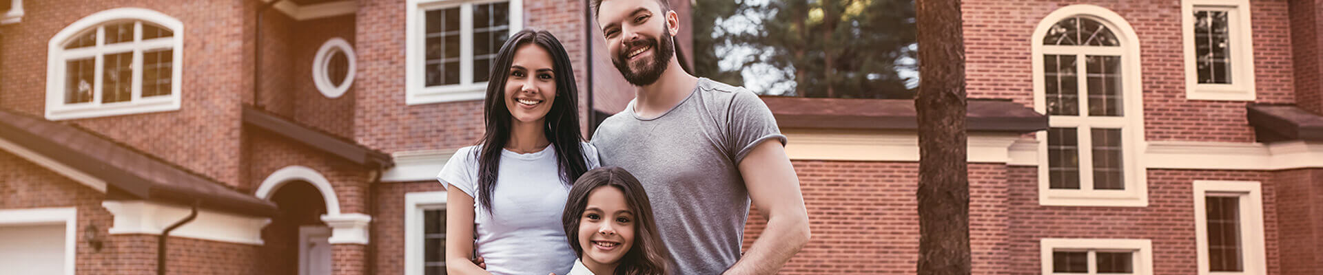 Happy mother, father, and small daughter standing in front of their home