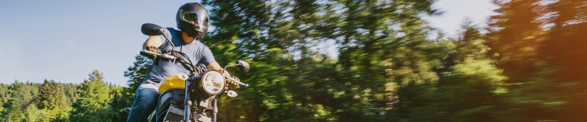 Motorcycle driver riding on tree-lined street on vintage motorcycle