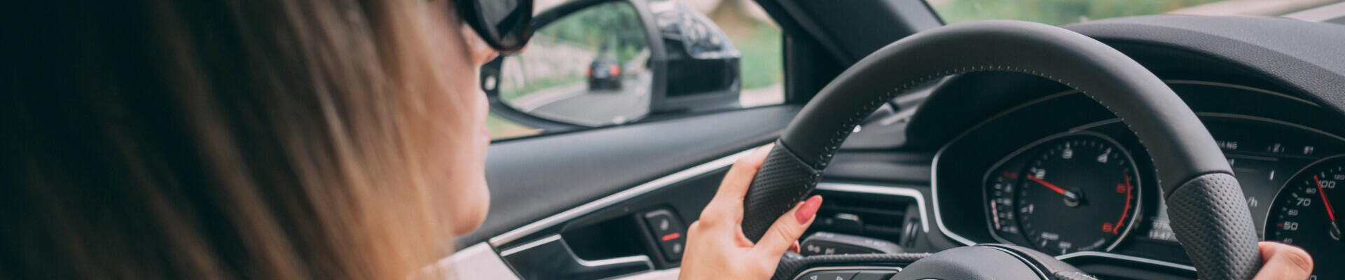 Close up of woman wearing sunglasses with hands on the steering wheel of a car