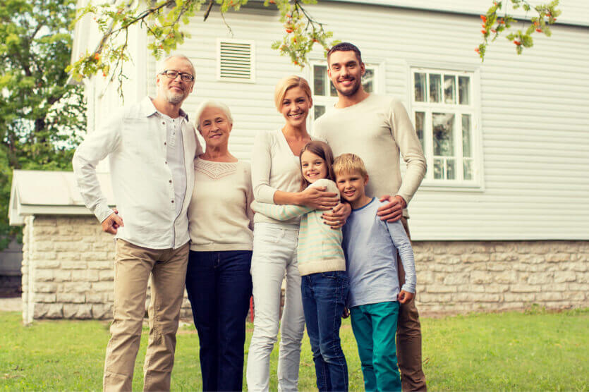 Happy parent, grandparents, and children standing in front of their home