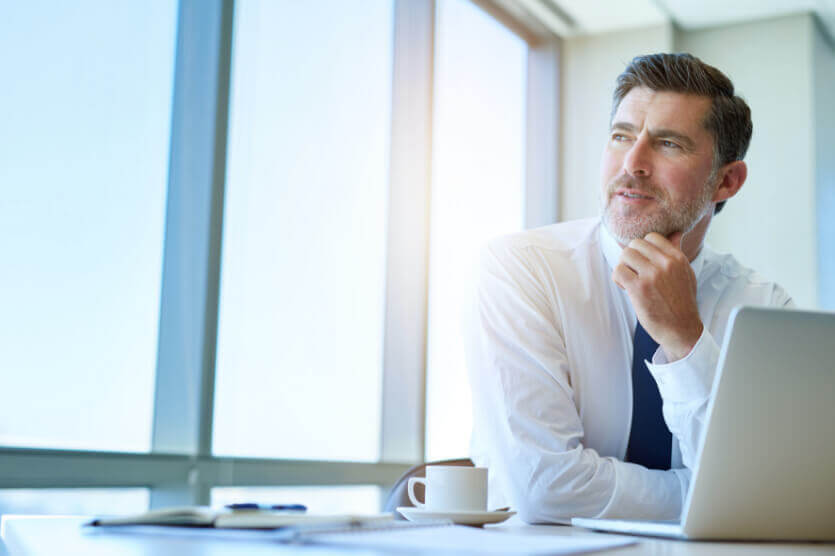 Business man in desk in front of laptop looking out the window