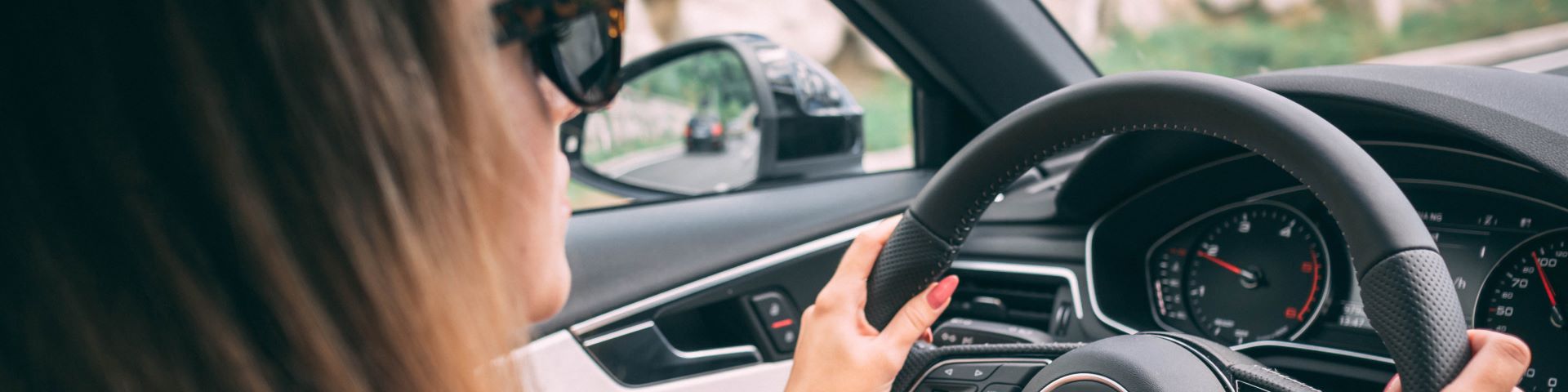 Close up of woman wearing sunglasses with hands on the steering wheel of a car.