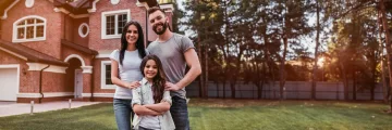 Happy mother, father, and small daughter standing in front of their home