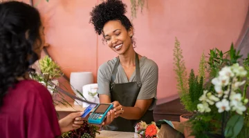 Smiling florist shop owner holds car reader to customer.