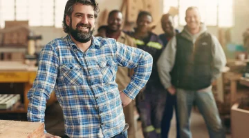 A smiling carpenter with his staff in the background