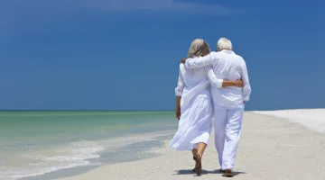 Rear view of a senior man and woman couple walking arms around each other on a deserted tropical beach