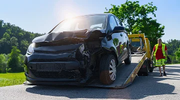 Damaged car being towed onto a flatbed tow truck with operator walking behind. Roadside assistance concept image.