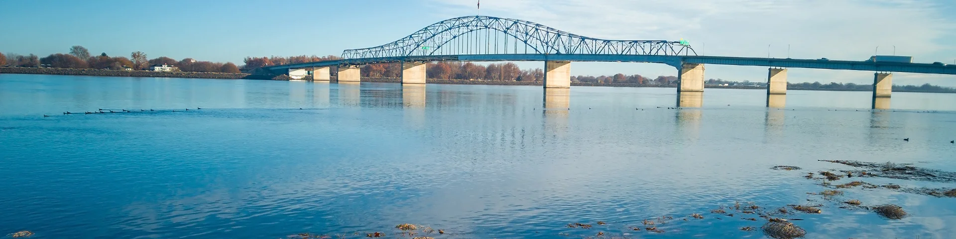 Historic blue and white arch truss bridge over the Columbia River with blue skies and clouds on a sunny morning in Kennewick-Pasco - best car insurance in Washington.