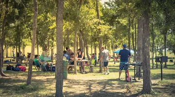 Blurred large group of friend, family members enjoy barbecue on lakeside area. Outdoor camping at natural park with picnic table in Grand Prairie - best home insurance in Florida.