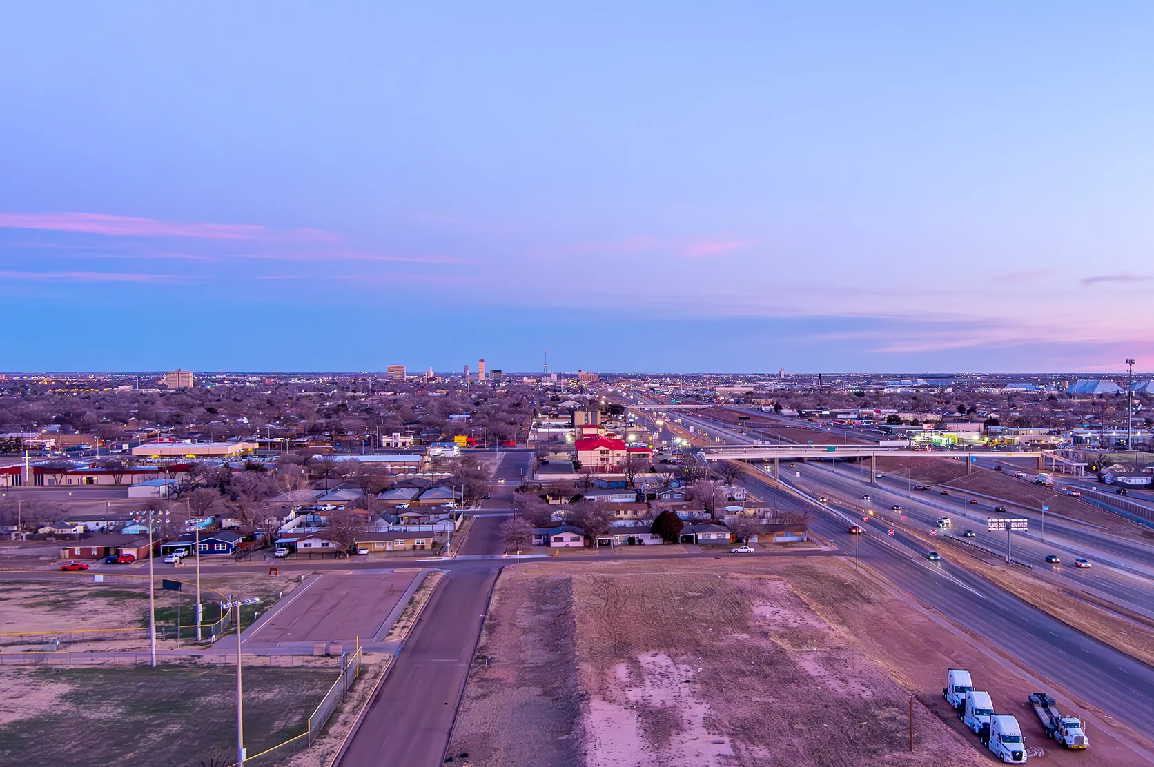 Aerial Cityscape of Lubbock Texas with traffic on the roads and tall buildings in the background against a blue sky at sunrise.