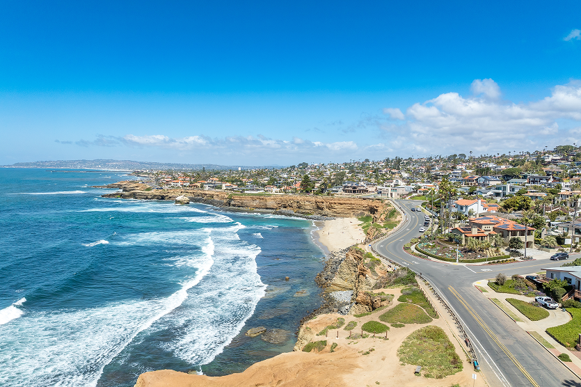 Aerial panorama of Sunset Beach in San Diego with ragged California ocean coastline, crushing waves, luxury single family homes and residences with pools.