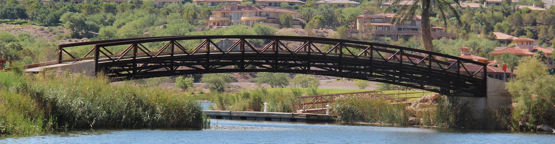 An oasis in the middle of the desert. A wooden bridge on the lake, vegetation, trees and in the background houses and Henderson-Nevada.
