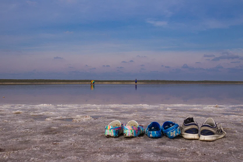 A selective focus shot of sandals on a salt beach. In the distance, people are visible interacting with the beach water at La Sal Del Rey in Edinburg - best homeowners insurance in Texas.