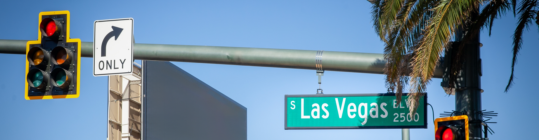 A typical American intersection on Las Vegas Boulevard (or las vegas strip), featuring traffic lights, road signs, and palm trees, symbolizing the urban landscape of Las Vegas, Nevada.