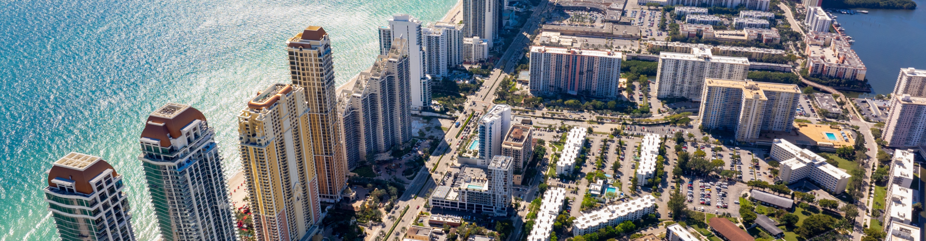 Aerial view of Miami Beach, Florida, showing a dense cluster of high-rise beachfront condominiums and hotels along a turquoise Atlantic coastline.
