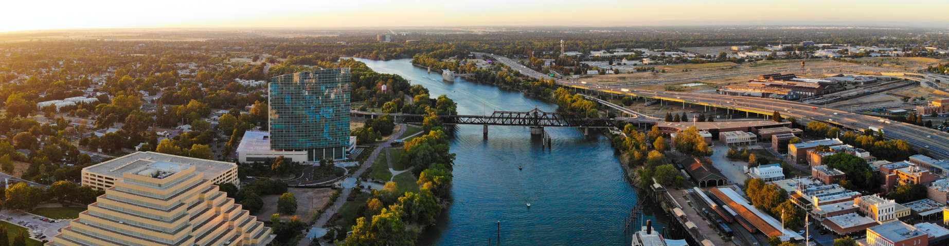 Aerial view of downtown Sacramento, California, featuring the Sacramento River, Tower Bridge corridor, waterfront districts, and surrounding commercial buildings at sunset.