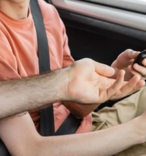 Parent handing car keys to a teenager inside a vehicle, illustrating the process of adding a teen driver car insurance policy.