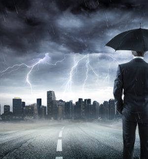 Businessman With Umbrella Looking Storm Over City, contemplating whether he needs umbrella insurance or liability insurance to protect his business.