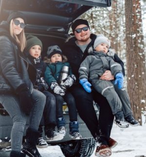 Young family sitting on their car trunk in a winter forest, highlighting the need for smart holiday travel insurance tips during cold-weather trips