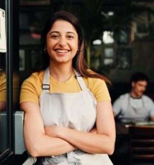 Small business owner smiles while standing at the entrance of her store with an open sign, highlighting independence and security backed by small business insurance.