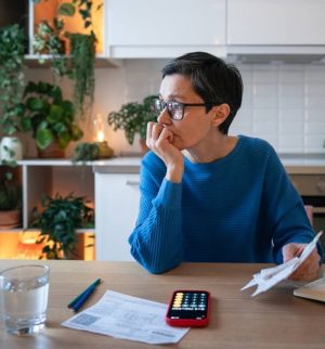 Concerned worried mature woman with bills and receipts, calculating budget and balancing expenses. Female facing debts, mismanagement of funds, rising utility price, tax increase and finance planning