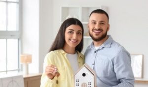 Happy couple holding house keys and a home model, representing homeowners insurance for new homebuyers.