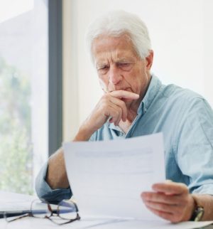Older man reviewing financial documents at a table with a laptop, representing retirement planning and protecting home assets.